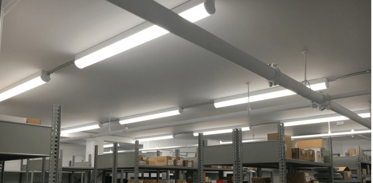 Linkable LED linear strip light fixtures illuminating a warehouse workspace